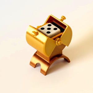 May include: A gold-colored miniature dice shaker with a white die showing five dots. The shaker has a barrel shape and sits on a copper-colored base. The lid is open, revealing the die inside. A fun game accessory.