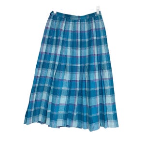 May include: A vintage, knee-length plaid skirt in shades of blue and teal, with a hint of purple. The skirt features a pleated design and a waistband with a belt loop. The fabric has a soft, textured appearance, and the skirt hangs from a white hanger.