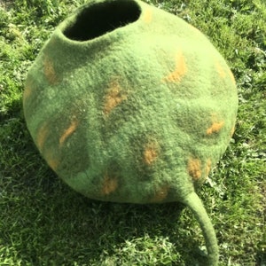Peut inclure: Un lit pour chat en feutre vert et orange avec une ouverture ronde et une longue queue.