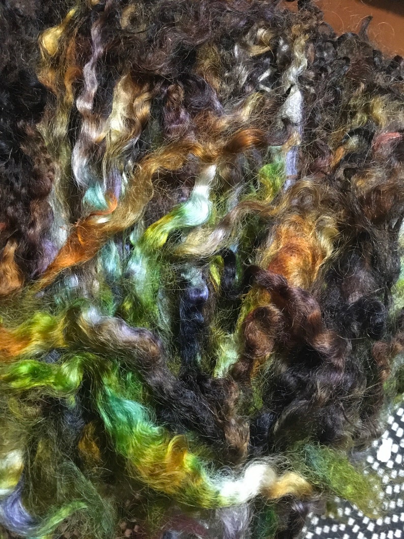 May include: A pile of colorful yarn in shades of brown, green, blue, and white. The yarn is soft and fluffy, and it would be perfect for knitting or crocheting.