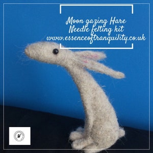Puede incluir: Un kit de fieltro con aguja para hacer un liebre beige con orejas rosas, ojos negros y cuello largo. El kit se llama "Moon Gazing Hare Needle Felting Kit" y el sitio web es www.essenceoftranquility.co.uk.