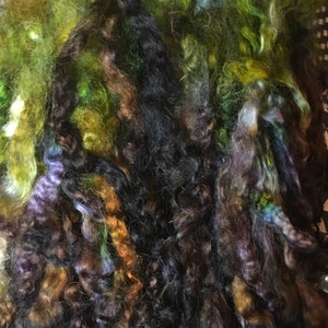 May include: A bundle of colorful yarn in shades of green, brown, black, and purple. The yarn is soft and fluffy, and it would be perfect for knitting or crocheting.