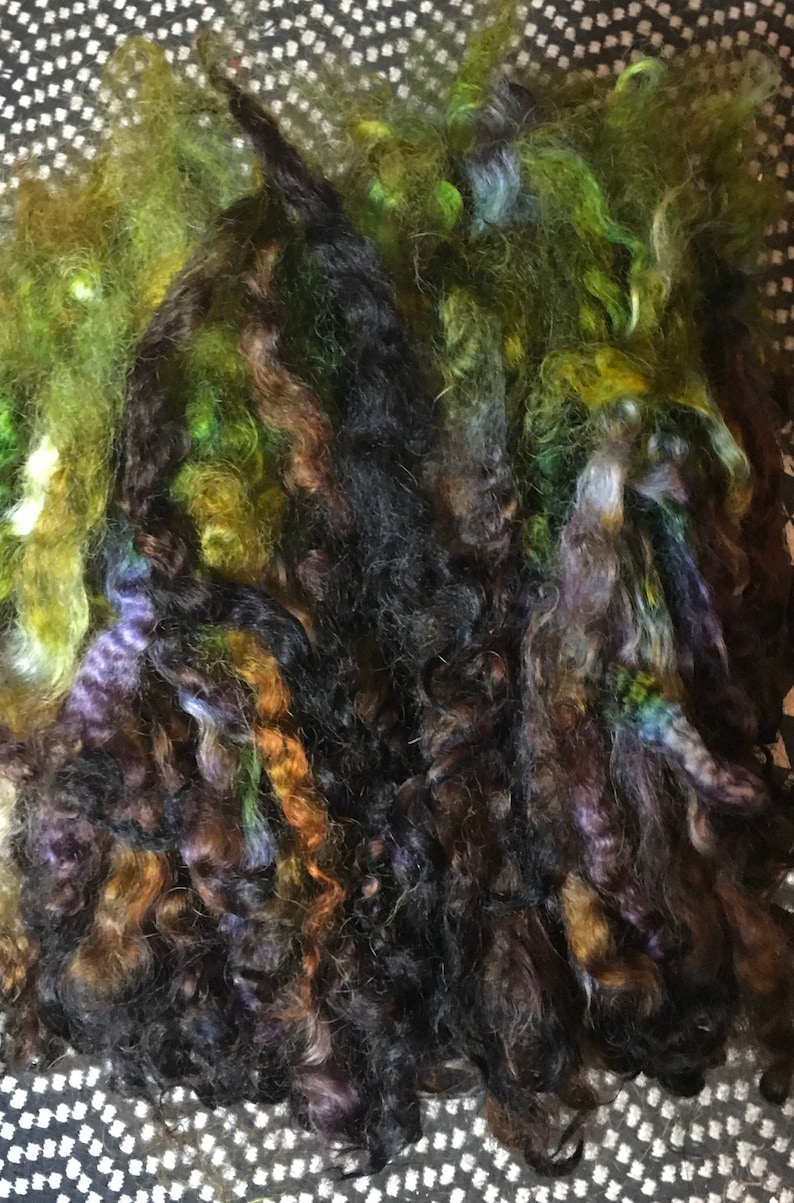May include: A bundle of colorful yarn in shades of green, brown, black, and purple. The yarn is soft and fluffy, and it would be perfect for knitting or crocheting.