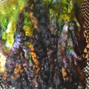 May include: A bundle of colorful yarn in shades of green, brown, black, and purple. The yarn is soft and fluffy, and it would be perfect for knitting or crocheting.