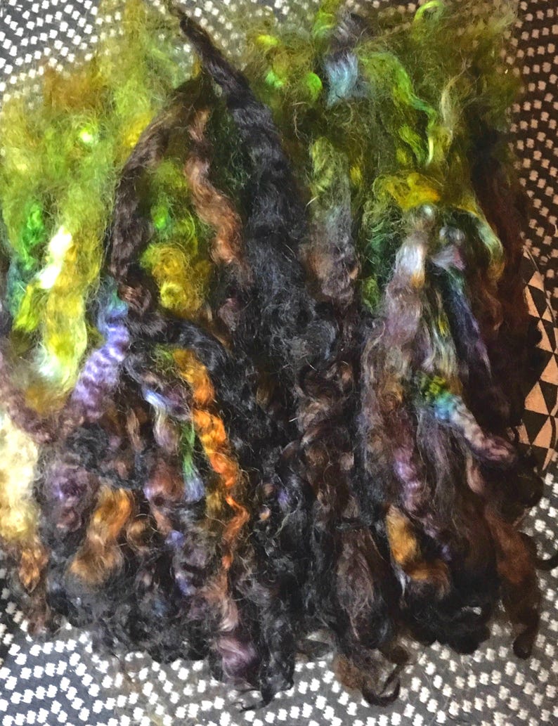 May include: A bundle of colorful yarn in shades of green, brown, black, and purple. The yarn is soft and fluffy, and it would be perfect for knitting or crocheting.
