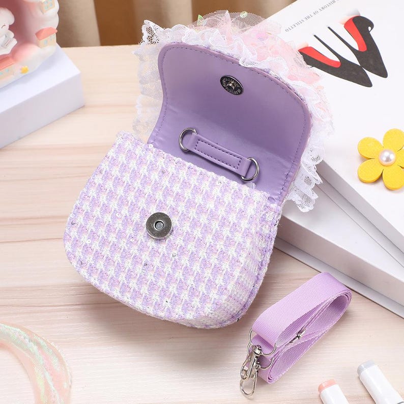 K&ouml;nnte beinhalten: Eine lilafarbene und wei&szlig;e Tweed-Handtasche mit Klappverschluss und Magnetknopf, verziert mit wei&szlig;er Spitzenborte am oberen Rand. Das Innere ist mit lilafarbenem Stoff gef&uuml;ttert und enth&auml;lt einen abnehmbaren, verstellbaren Schulterriemen.
