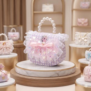 K&ouml;nnte beinhalten: Eine lavendelfarbene und wei&szlig;e Tweed-Handtasche mit einem Perlenhenkel, wei&szlig;er Spitzenborte und einer zentralen rosa T&uuml;llschleife, die mit einer kleinen Elsa-Figur aus dem Film Die Eisk&ouml;nigin auf der Vorderseite verziert ist.