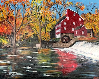 May include: A red gristmill with a water wheel sits on a river in a forest with fall foliage. The water wheel is turning and the river is flowing over a small waterfall.