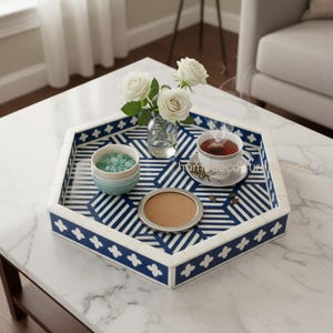 Könnte beinhalten: Sechseckiges Serviertablett mit blau-weißem geometrischen Muster. Das Tablett enthält eine Teetasse, eine kleine Schüssel, einen Untersetzer und eine Vase mit weißen Rosen. Das Tablett hat einen weißen Rand mit blauen Blumenakzenten.