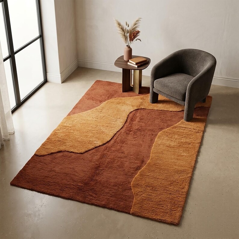 Abstract terracotta and mustard wool rug styled near an accent chair, highlighting its warm earthy palette and sculptural organic pattern.