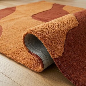 Folded-edge view of the hand-tufted wool rug showing its textured pile, layered surface, and terracotta brown and mustard ochre color blocks.