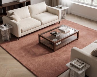 May include: A large rectangular area rug in a solid terracotta color with a textured pile surface. The rug is positioned beneath a glass-topped coffee table with a wooden frame, two cream-colored sofas, and several marble side tables.