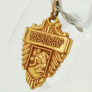 May include: Gold-coloured wrestling charm with a wrestler in a fighting pose and the text "WRESTLING 154 POUNDS".