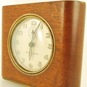 May include: A vintage Seth Thomas clock in a rectangular wooden case. The clock face is white with black numerals and hands, framed by a gold-coloured bezel. It features a small seconds dial. A classic timepiece.