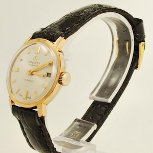 May include: A gold-tone wristwatch with a white face and black leather strap. The watch face has gold-tone hands and markers, and the text "Tressa 17 Jewels Incabloc" is printed on the face.