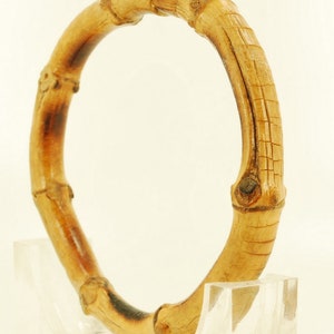 May include: A natural bamboo bangle bracelet. The bracelet is made of multiple pieces of bamboo that have been joined together to form a circle. The bamboo is a light brown color and has a natural, rustic finish.