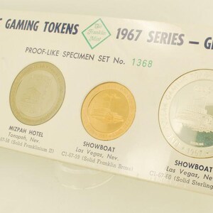 May include: A 1967 series proof-like specimen set of domestic gaming tokens. The set includes four tokens: Big Bonanza, Mizpah Hotel, and two Showboat tokens. The tokens are in gold and silver tones, with text on the tokens and the packaging.