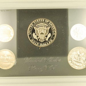 May include: A United States Proof Set in a clear plastic case. The set includes a half dollar, a quarter, a dime, a nickel, and a penny. The coins are displayed against a black background, with the words "United States Proof Set" visible.