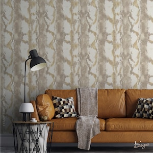 K&ouml;nnte beinhalten: Ein beiges Ledersofa mit einer grauen Decke und zwei karierten Kissen vor einer Wand mit wei&szlig;-goldener Schlangenhaut-Tapete. Eine schwarze Lampe steht auf einem Draht-Beistelltisch mit dem aufgedruckten Text I need more sleep.