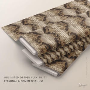 Puede incluir: Una tela doblada con un patr&oacute;n realista de piel de serpiente en tonos marr&oacute;n, beige y crema. El material muestra una textura detallada de escamas repetitivas en toda su superficie, presentada en una pila con bordes blancos visibles.