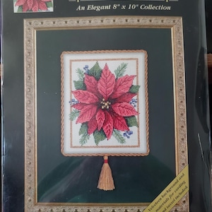May include: A cross-stitch kit featuring a poinsettia design. The framed artwork measures 8 inches by 10 inches. The image shows a red poinsettia with green leaves and blue berries, with a gold tassel and frame.