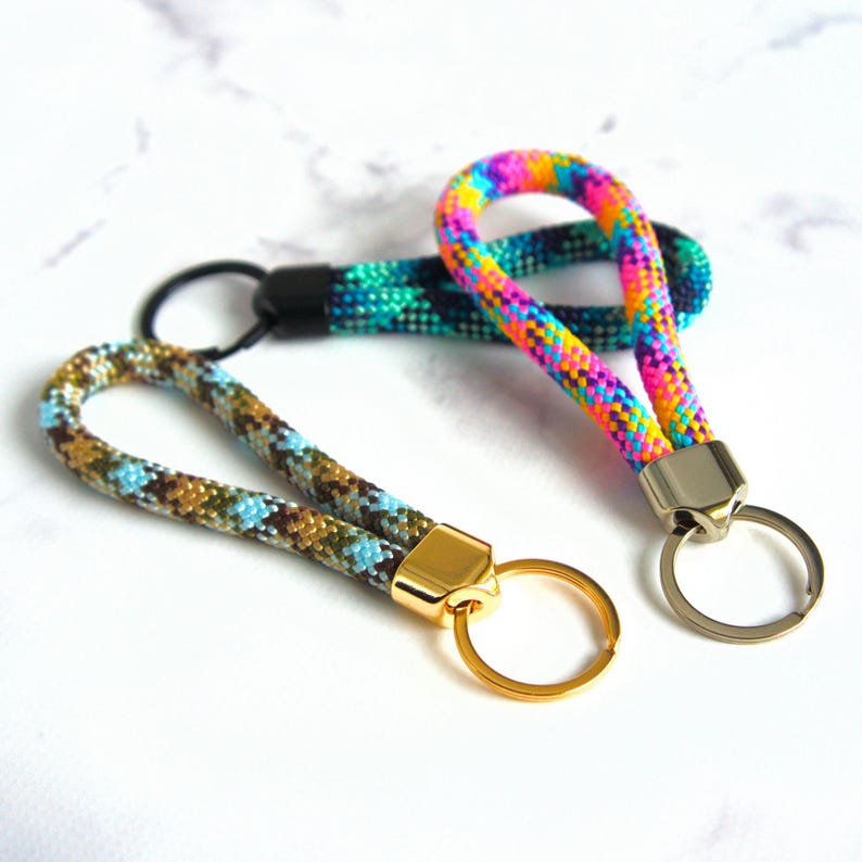 Pode incluir: Tr&ecirc;s chaveiros com cord&otilde;es tecidos coloridos. Um chaveiro tem um padr&atilde;o de arco-&iacute;ris, outro tem um padr&atilde;o turquesa e preto, e o terceiro tem um padr&atilde;o castanho, azul e bege. Cada chaveiro tem um anel e um fecho de metal.