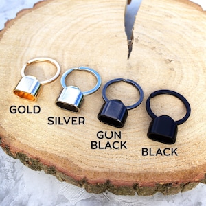 May include: Four metal keychains in gold, silver, gun black, and black. Each keychain has a ring and a rectangular cap. The word "GOLD", "SILVER", "GUN BLACK", and "BLACK" are printed below each keychain.