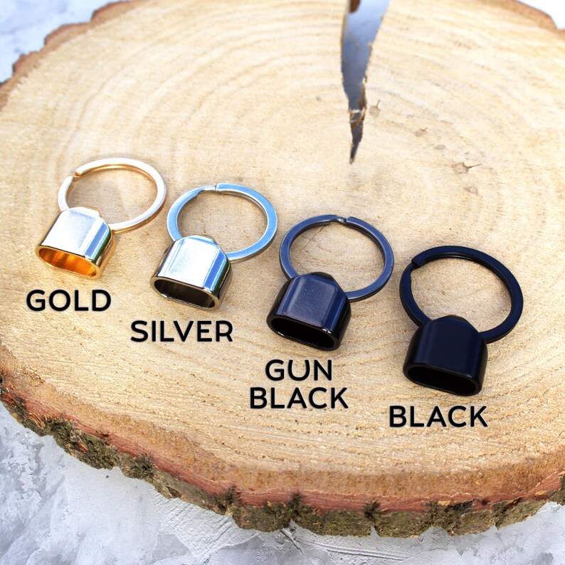 May include: Four metal keychains in gold, silver, gun black, and black. Each keychain has a ring and a rectangular cap. The word "GOLD", "SILVER", "GUN BLACK", and "BLACK" are printed below each keychain.