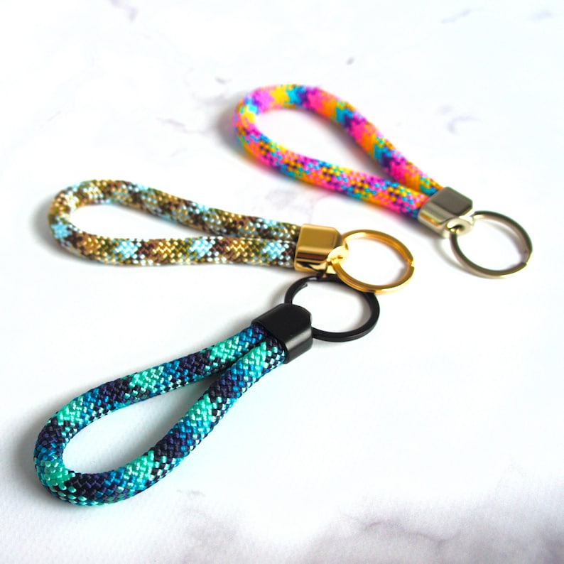 May include: Three colorful wrist keychains. One is a rainbow of pink, yellow, and blue. Another is a mix of green, brown, and blue. The third is a mix of blue and green. Each keychain has a metal clasp and ring.