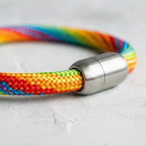 Peut inclure: Un bracelet en corde multicolore avec un fermoir magnétique argenté. Le bracelet présente un éventail de couleurs vives, dont le rouge, l'orange, le jaune, le vert, le bleu et le violet. Le fermoir est de forme cylindrique.