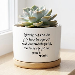 以下が含まれることがあります： 多肉植物が入った白いセラミックプランター。 プランターは木製のベースで、「友情はあなたが最も長く知っている人についてではありません...」と下部に「Jessica」という名前が書かれた黒いスクリプトが特徴です。
