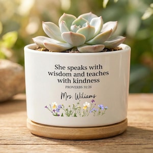 May include: White ceramic planter with a succulent plant. The planter has the text "She speaks with wisdom and teaches with kindness PROVERBS 31:26 Mrs. Williams" and a floral design. The planter sits on a wooden base.