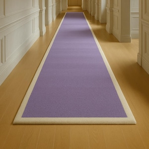 May include: A long, rectangular purple rug with a cream-colored border. The rug is placed in a hallway with light-colored walls and a wooden floor. The rug's dimensions are not visible.