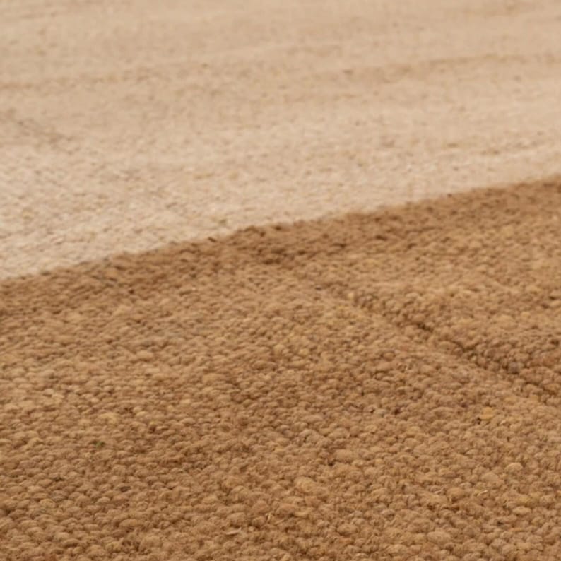 May include: Close-up of a textured rug with a diagonal color block design. The rug features two shades of brown, with a lighter tan color in the upper portion and a darker brown in the lower portion. The rug has a woven texture.