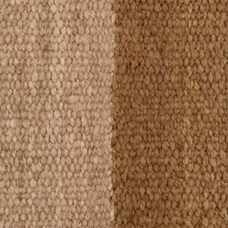 May include: Close-up of a textured rug with two vertical sections. One section is a light tan color, and the other is a medium brown. The rug has a woven appearance, with visible fibers and a nubby texture.