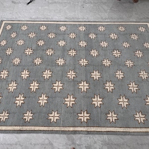 May include: A rectangular, blue area rug with a repeating pattern of off-white starburst designs. The rug has a cream-colored border and fringe along the edges. The rug is made of a woven material.