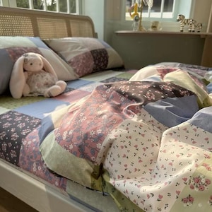 May include: A bed with a patchwork quilt featuring floral patterns in pink, white, and green. A plush bunny toy with long ears sits on the bed, which has a woven headboard and patchwork pillows.