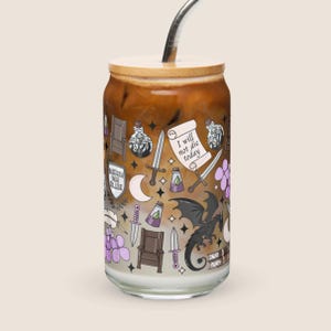 May include: A clear glass can-shaped tumbler with a bamboo lid and a stainless steel straw. The tumbler is filled with a layered drink and decorated with fantasy-themed illustrations, including swords, a dragon, and the text "I will not die today."