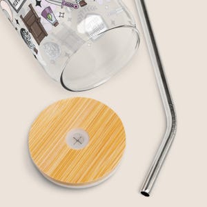 May include: A clear glass tumbler with a bamboo lid and a stainless steel straw. The tumbler is decorated with whimsical illustrations. The lid is round and made of light brown bamboo. The straw is silver and bent at the top.