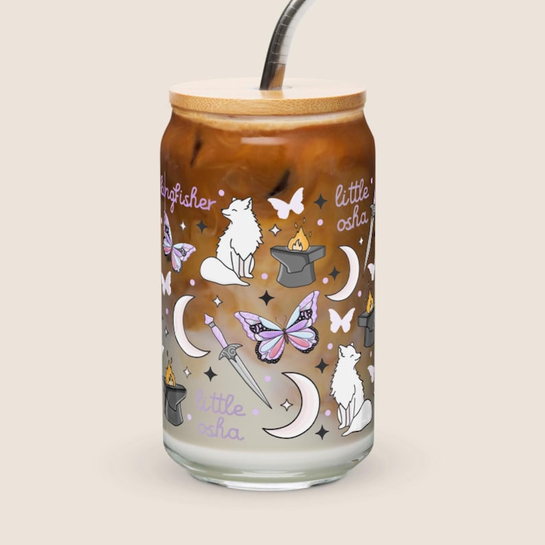 May include: A glass iced coffee cup with a bamboo lid and a metal straw. The cup is decorated with whimsical illustrations of white foxes, butterflies, moons, a sword, and the text "kingfisher" and "little osha".
