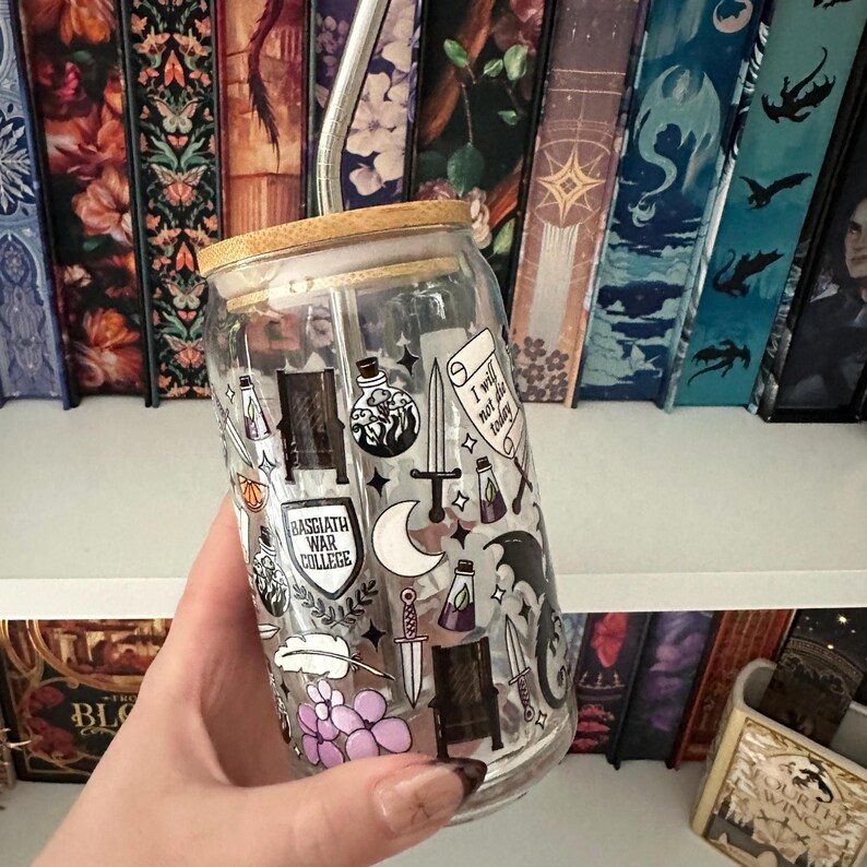 May include: A clear glass tumbler with a bamboo lid and a stainless steel straw. The tumbler is decorated with fantasy-themed illustrations, including swords, potions, and the text "BASGIATH WAR COLLEGE" and "I will not die today".