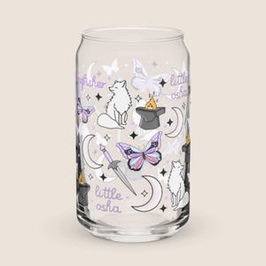 May include: A clear glass can-shaped drinking glass with a whimsical design. The design includes white foxes, butterflies, moons, stars, a sword, and the text "kingfisher" and "little osha" in a purple script. The butterflies have pink, purple, and blue wings.