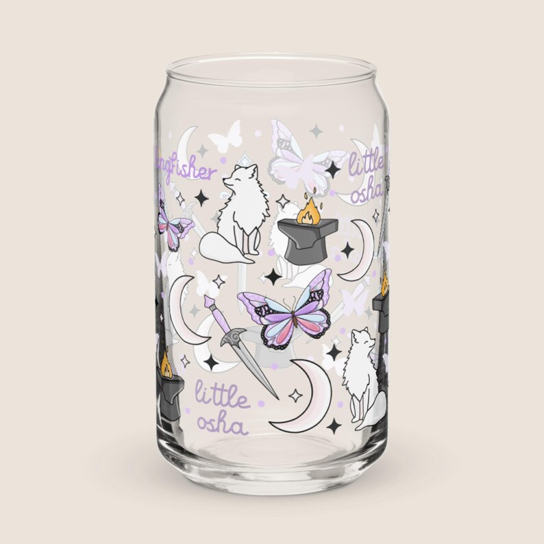 May include: A clear glass can-shaped drinking glass with a whimsical design. The design includes white foxes, butterflies, moons, stars, a sword, and the text "kingfisher" and "little osha" in a purple script. The butterflies have pink, purple, and blue wings.