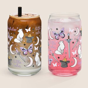 May include: Two glass beverage cups with decorative designs. One cup contains a coffee drink with a black straw, the other a pink beverage. Both feature illustrations of butterflies, swords, moons, and foxes, with the text "little osha".