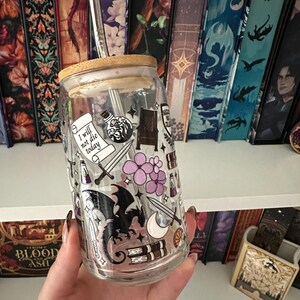 May include: A clear glass tumbler with a bamboo lid and a stainless steel straw. The tumbler is decorated with fantasy-themed stickers, including a dragon, swords, and the text "I will not die today".
