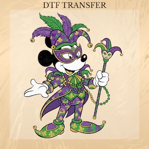 May include: DTF TRANSFER text above a cartoon image of Mickey Mouse in a Mardi Gras jester costume. The character wears a purple and green outfit with a matching hat, mask, and staff. The design includes fleur-de-lis patterns and beaded necklaces.