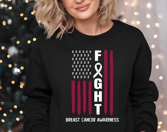 May include: Black sweatshirt with a design featuring the word "FIGHT" in white, with a pink ribbon and stripes. The design includes the text "BREAST CANCER AWARENESS" at the bottom. The sweatshirt is a crew neck.