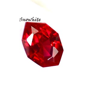 Può includere: Una gemma rossa vibrante e sfaccettata con un taglio geometrico complesso. La gemma riflette la luce, creando riflessi e ombre brillanti. La parola "Snowwhite" è scritta in corsivo sopra la gemma. Su sfondo bianco.