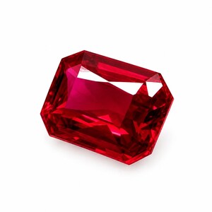 May include: A vibrant, deep red gemstone with a rectangular emerald cut. The stone features sharp, clean facets that create internal light reflections and a high-gloss, transparent finish, showcasing a rich, saturated crimson color throughout.