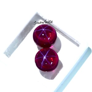 May include: Two round, deep red gemstones with a star-like pattern, set against a white background. The gemstones have a polished, reflective surface. The word "Snowwhite" is written in the upper left corner.